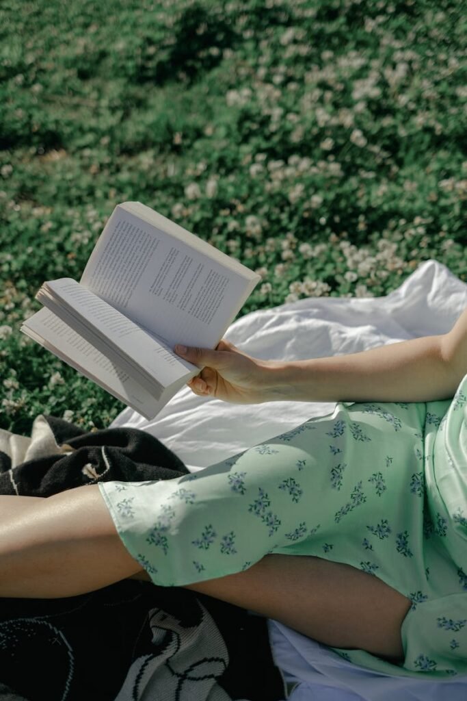 A woman in a floral dress enjoys a sunny day reading a book outdoors.