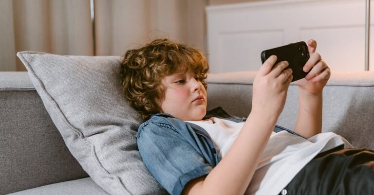 Young boy relaxing on a sofa, using a smartphone, indoors.