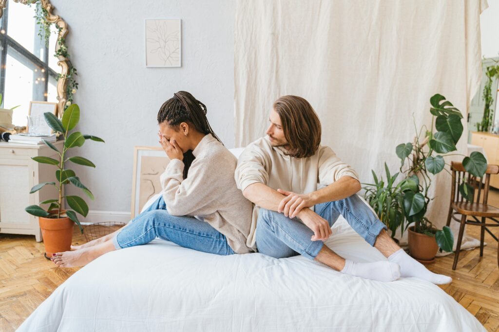Couple sitting back-to-back on bed, showing relationship conflict in a cozy room.